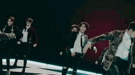 a group of young men are dancing together on a stage in a dark room .