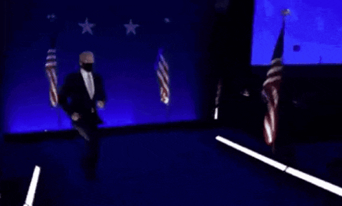 a man in a suit is dancing on a stage in front of american flags