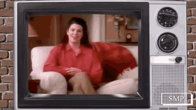 a woman in a red shirt is sitting on a couch in front of a television screen .