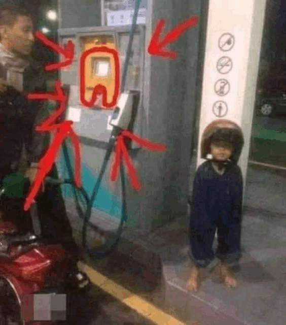 a little boy wearing a helmet is sitting on the ground at a gas station .