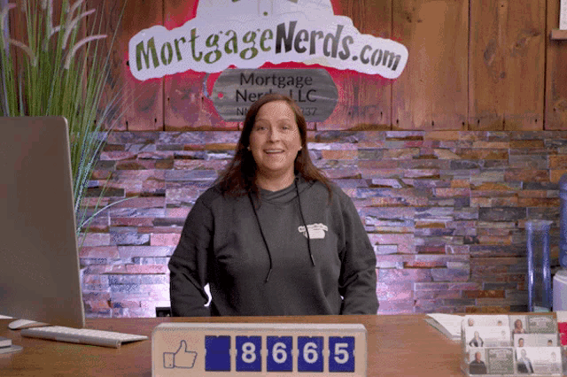 a woman sitting at a desk in front of a mortgage nerds.com sign