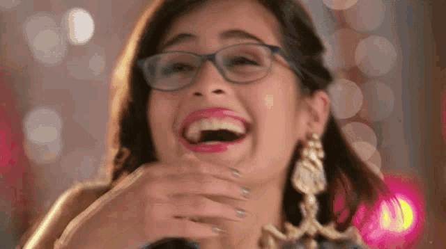 a woman wearing glasses is laughing with her mouth open and covering her face .