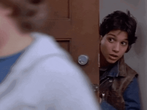 a man in a denim vest is peeking out of a doorway .