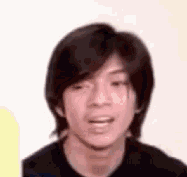 a young man with long dark hair is making a funny face .