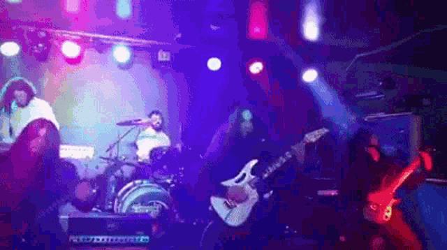 a man playing a guitar in front of a drum set with purple lights