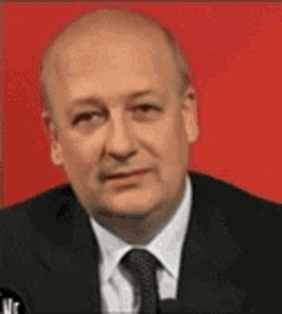 a man in a suit and tie is sitting in front of a red wall .
