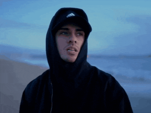 a man wearing a black hoodie and a hat with the word adidas on it