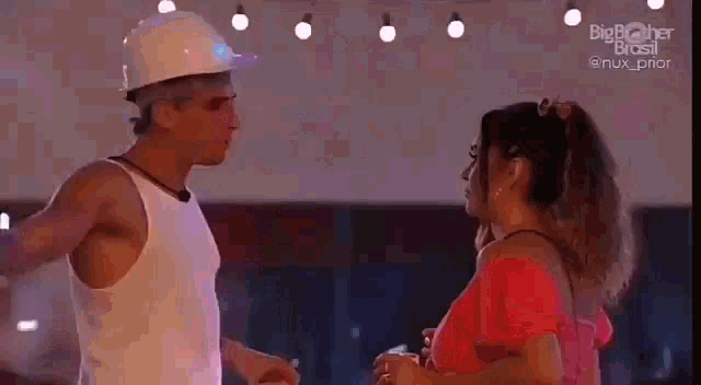 a man and a woman are standing next to each other in a room . the man is wearing a hard hat .