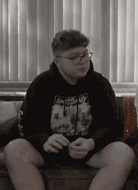 a young man wearing a hoodie that says ghost on it sits on a couch