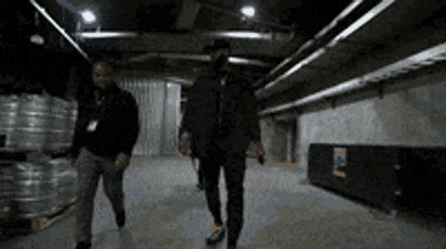 two men are walking in a dark warehouse with a sign that says ' e ' on it