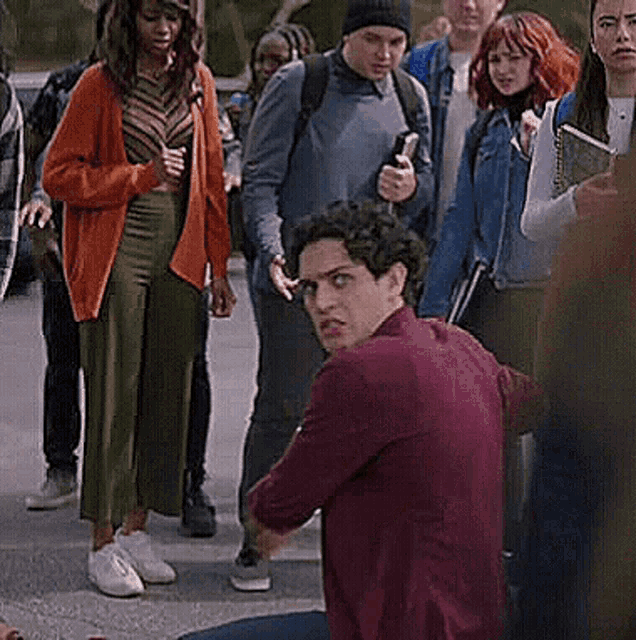 a group of people are standing around a man in a red jacket kneeling on the ground .