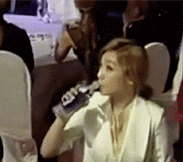 a woman is drinking water from a bottle while sitting in a chair
