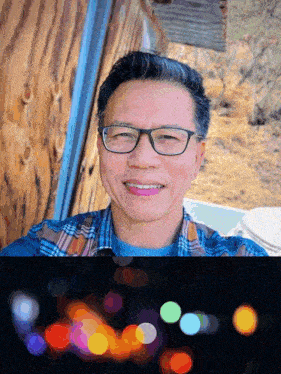 a man wearing glasses and a plaid shirt smiles in front of a wooden wall