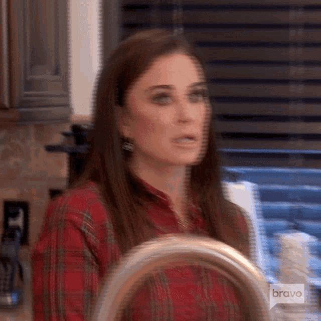 a woman in a plaid shirt is standing in front of a sink in a kitchen .