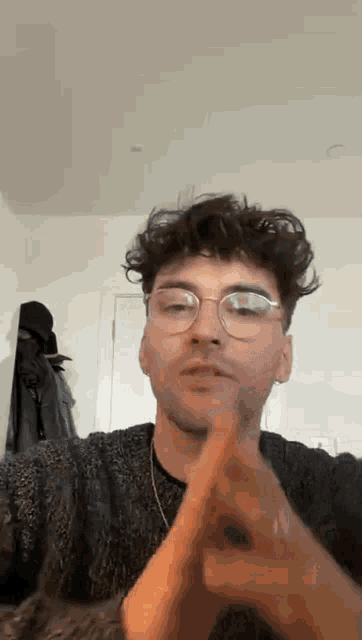 a young man wearing glasses and a sweater is making a peace sign .