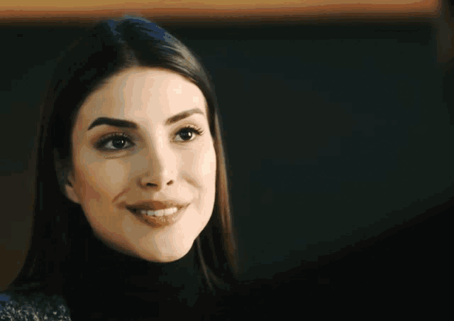 a woman wearing a black turtleneck is smiling for the camera