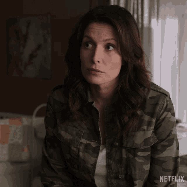 a woman in a camo jacket is sitting in front of a window with a netflix logo in the corner