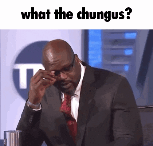 a man in a suit and tie is sitting in front of a sign that says " what the chungus "