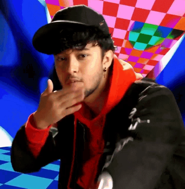 a man wearing a black hat and a red hoodie has his hand to his mouth