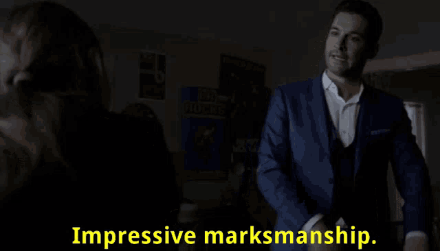 a man in a suit stands in a dark room with the words impressive marksmanship written on the bottom