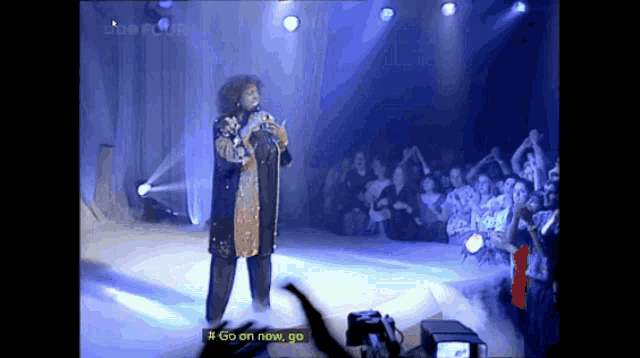 a woman singing on a stage with the words go on now go visible