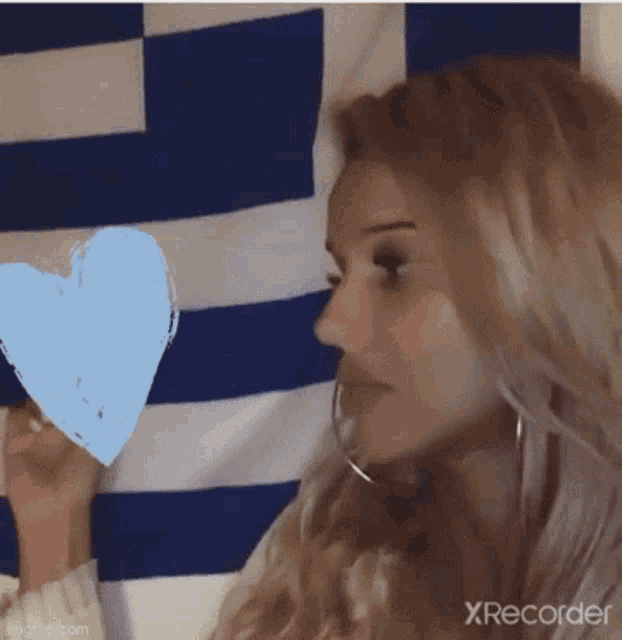 a woman is holding a heart in front of a blue and white striped flag .