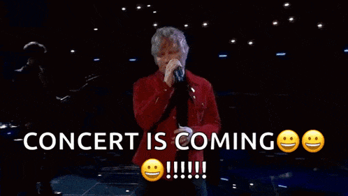 a man is singing into a microphone with the words concert is coming behind him .