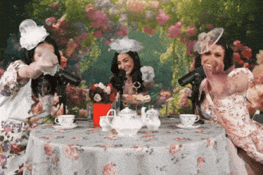 three women are sitting at a table with a teapot and cups