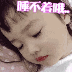 a little girl is sleeping in a bed with chinese writing on her face