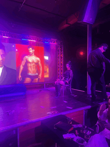a man in calvin klein underwear stands on a stage in front of a large screen