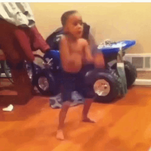 a young boy is standing in front of a toy car on a wooden floor .