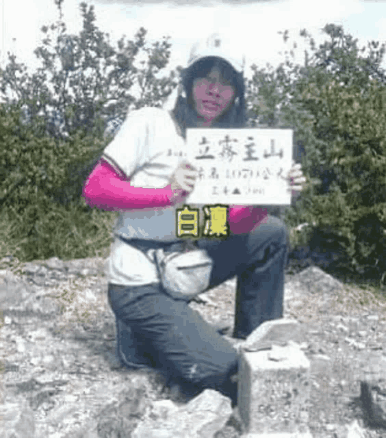 a woman is kneeling on a rock holding a sign that says ' taiwan ' on it .