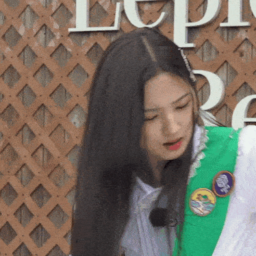 a girl with long black hair is wearing a green vest and a white shirt .
