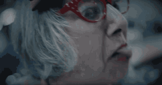 a woman wearing red glasses and red lipstick makes a funny face