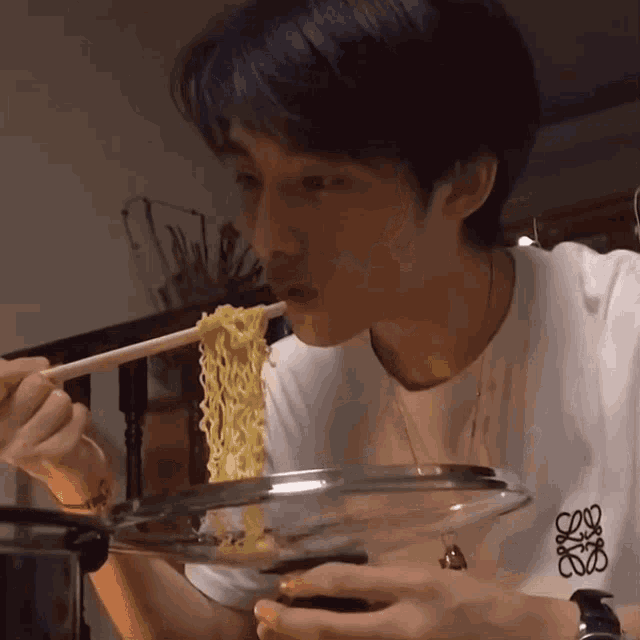 a man wearing a loewe shirt is eating noodles