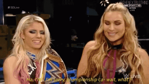 two women are sitting next to each other on a wrestling show and one of them is holding a championship belt .