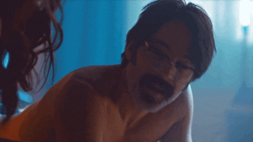 a shirtless man with glasses is laying on a woman 's lap