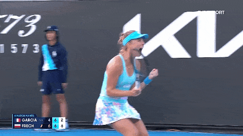 a woman in a blue tank top is holding a tennis racquet in front of a kia sign .