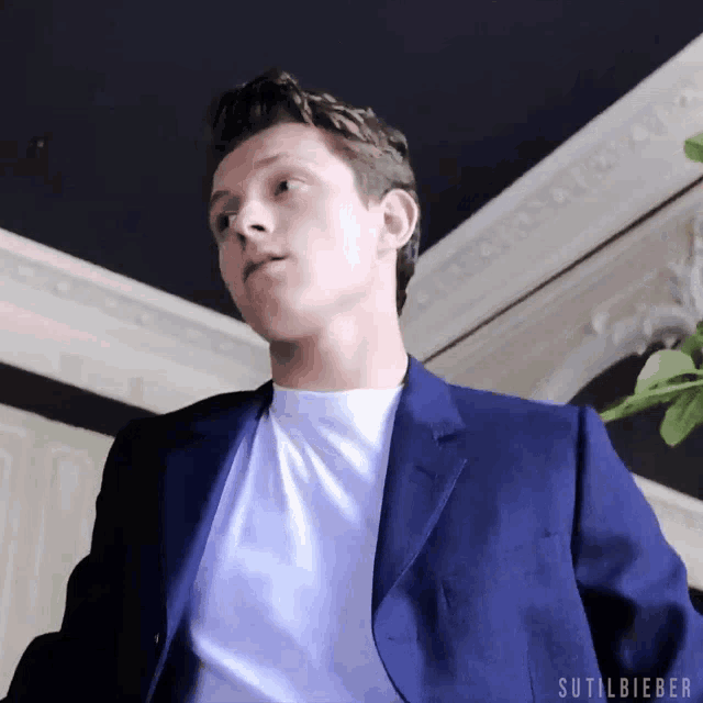 a young man in a blue suit and white shirt is standing in a room