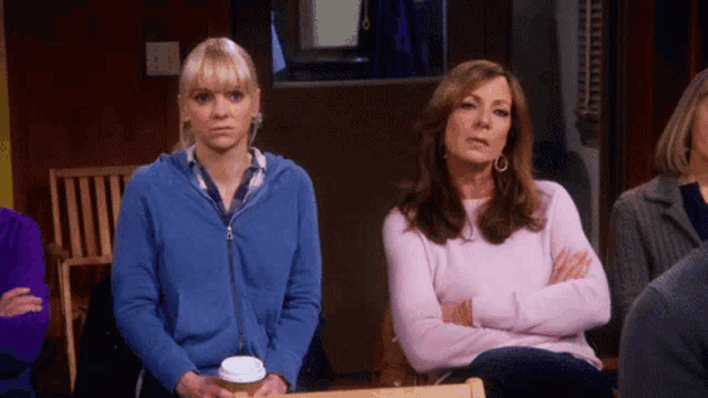 a woman in a pink sweater sits next to another woman in a blue sweatshirt