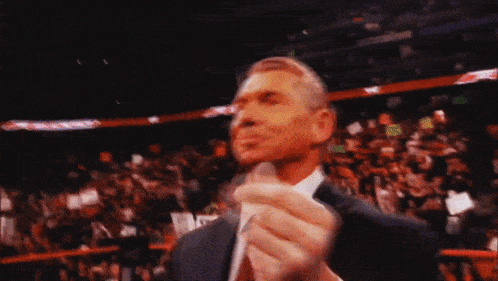 a man in a suit and tie stands in front of a crowd with a sign that says ' wwe ' on it