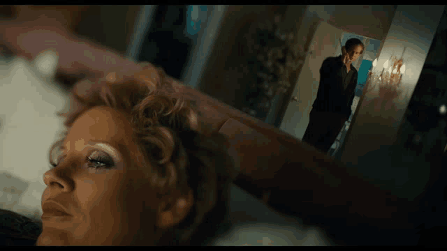 a woman is laying on a bed with a man standing in the background