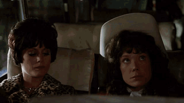 two women are sitting in the back seat of a car and one is wearing a white hat