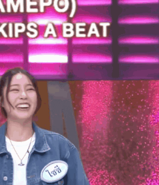 a woman in a denim jacket is smiling in front of a sign that says " kips a beat "