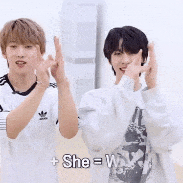 a couple of young men are standing next to each other and making a heart shape with their hands .