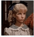 a young girl with blonde hair and a blue bow in her hair is looking at the camera .