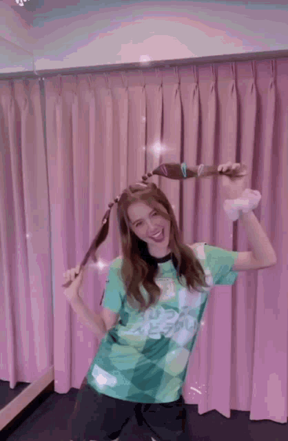 a woman in a green shirt is holding a broom in front of pink curtains