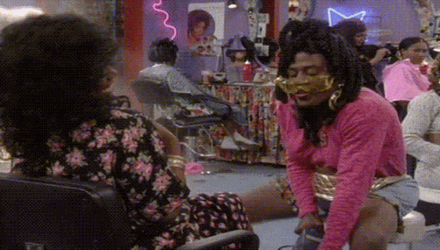a woman in a floral dress is sitting next to a man in a pink shirt in a salon .