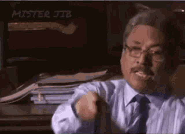 a man in a suit and tie is pointing at the camera while sitting at a desk .