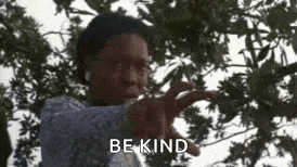 a man is standing in front of a tree and pointing at the camera with the words `` be kind '' behind him .
